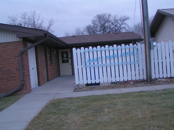 Huelett Park Apartments Sign and White Fence with Apartment door in the background